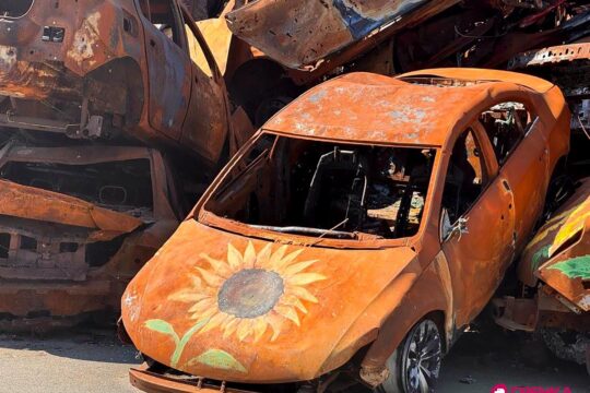 En mémoire des victimes de la guerre à Irpin (Ukraine), des monuments et des projets artistiques sont mis en place. Photo : des épaves de voitures calcinées et jaunies sont entassées. Des tournesols sont peints dessus.
