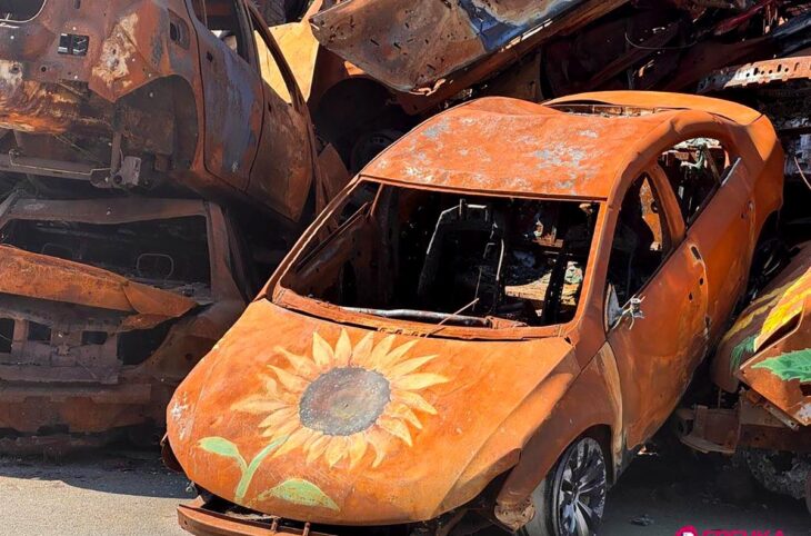 En mémoire des victimes de la guerre à Irpin (Ukraine), des monuments et des projets artistiques sont mis en place. Photo : des épaves de voitures calcinées et jaunies sont entassées. Des tournesols sont peints dessus.