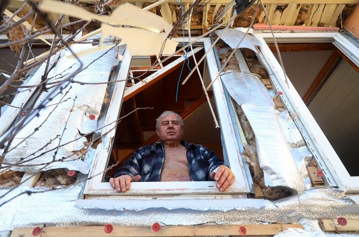 A man stands at the window of his partially destroyed house