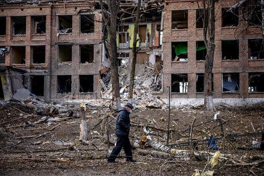 Un homme marche devant un bâtiment détruit