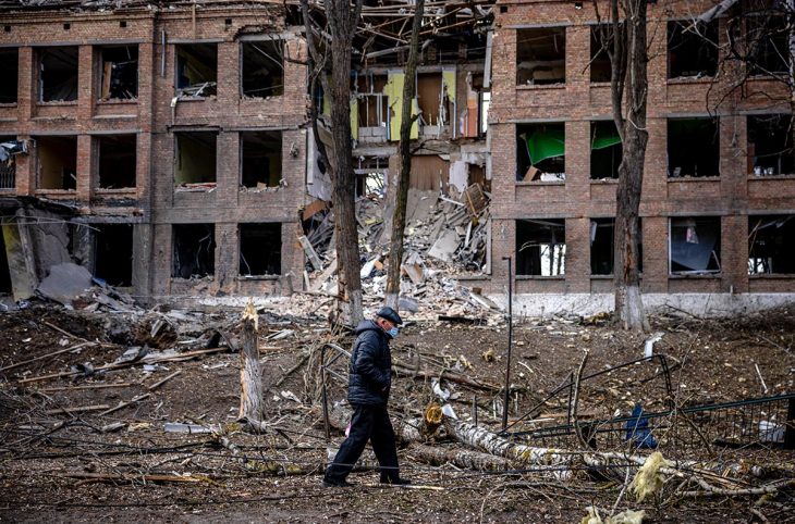A man walks in front of a destroyed building