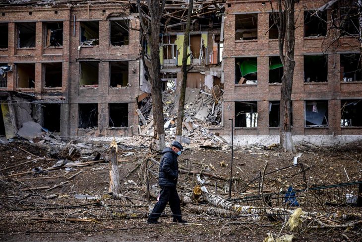 A man walks in front of a destroyed building
