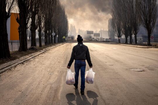 Procès d'un soldat russe pour crimes de guerre près de Kyiv, en Ukraine - Photo : un civil ukrainien marche dans la rue alors que des fumées sont visibles au loin, suite à un bombardement russe.