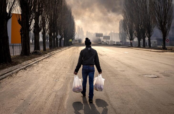Trial of a Russian soldier for war crimes near Kyiv, Ukraine - Photo: a Ukrainian civilian walks down the street while smoke is visible in the distance following a Russian shell strike.