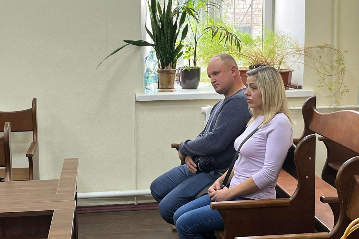 A man and a woman sit side by side on a bench in the courtroom of the in absentia trial of Russian soldier Serhiy Steiner in Ukraine.