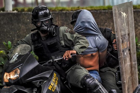 Deux policiers anti-émeute arrêtent un manifestant et l'emmènent sur une moto