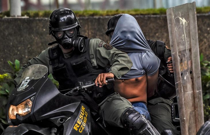 Two riot police officers arrest a protester and take him away on a motorbike