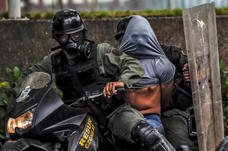 Two riot police officers arrest a protester and take him away on a motorbike