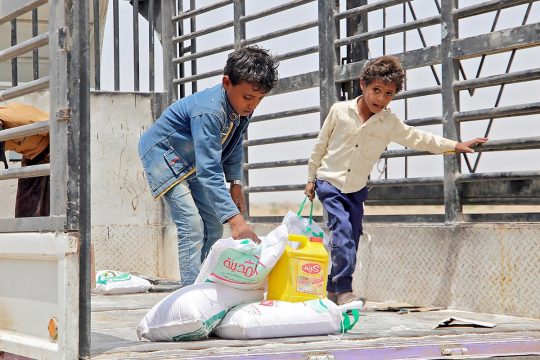 Two Yemeni children take the last bags of food from a truck as part of a feeding program.