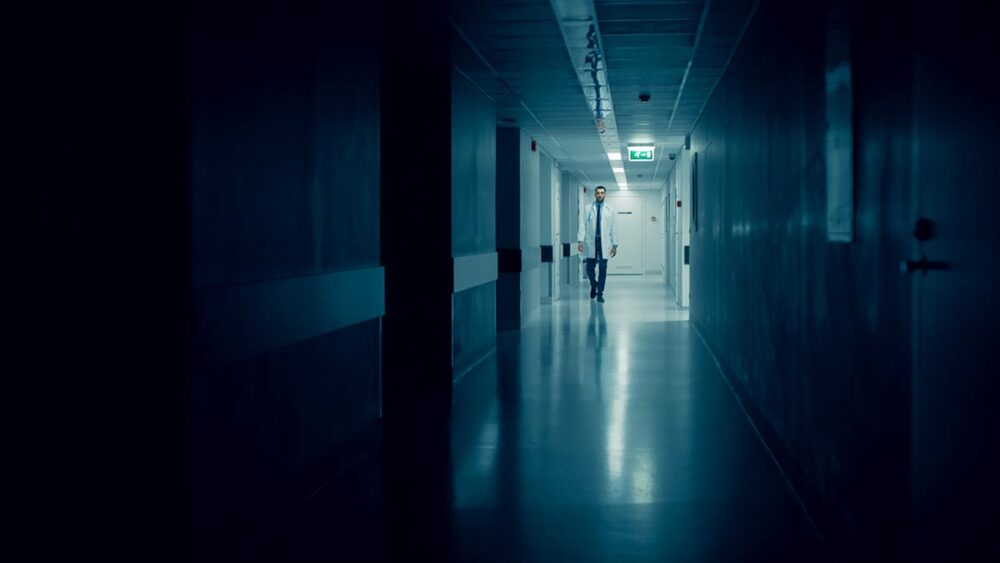 A doctor walks through the dark corridor of a hospital