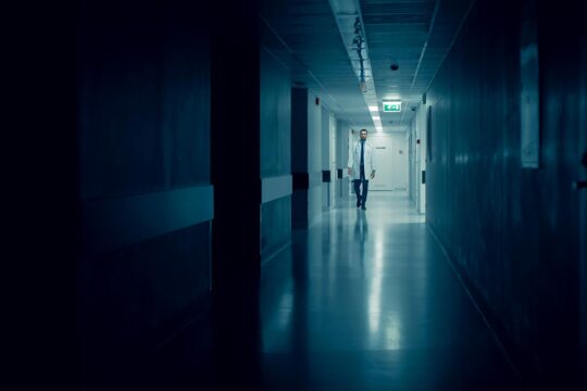 A doctor walks through the dark corridor of a hospital