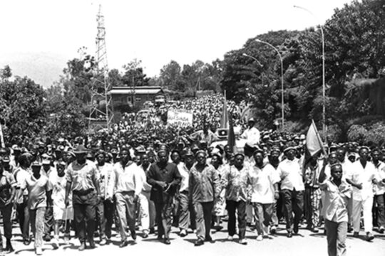 Le 26 octobre 1992, des miliciens Interahamwe et des militants extrémistes du MRND marchent dans le quartier populaire de Nyamirambo à Kigali pour manifester leur soutien aux Forces armées rwandaises (FAR). Une pancarte est brandie derrière, on y lit : « Interahamwe = victoire du MRND ».