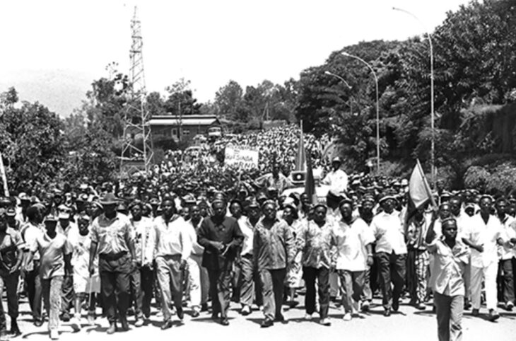 Le 26 octobre 1992, des miliciens Interahamwe et des militants extrémistes du MRND marchent dans le quartier populaire de Nyamirambo à Kigali pour manifester leur soutien aux Forces armées rwandaises (FAR). Une pancarte est brandie derrière, on y lit : « Interahamwe = victoire du MRND ».