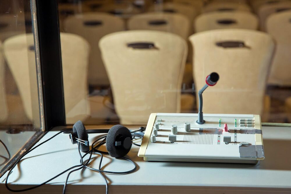 Translation of universal jurisdiction trials - Photo: instant translation equipment with microphone and headphones, in an insulated glass booth.